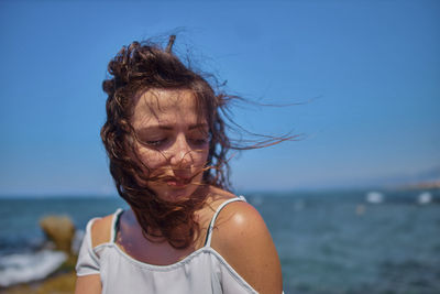 Close-up of young woman with tousled hair against sea and clear sky