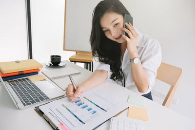 Young woman using phone while sitting on table
