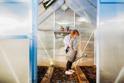 Young girl alone in backyard greenhouse watering seeds in spring