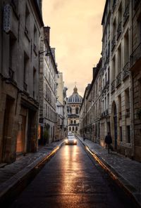 Empty road amidst buildings against sky during sunset in paris