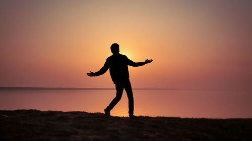 Silhouette man standing on shore against sky during sunset