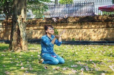 Young woman using phone while sitting on tree