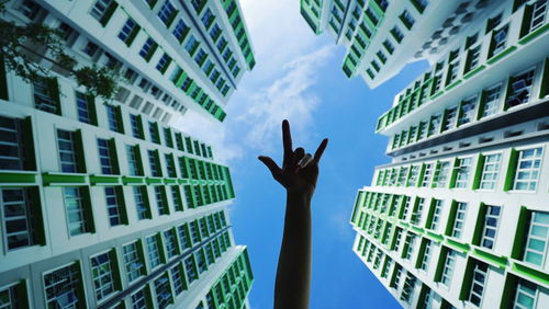 Cropped image of person with rock music sign amidst buildings against sky