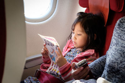 Girl reading paper while sitting with mother in airplane