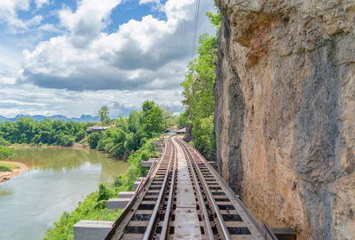 Railroad tracks by river against sky