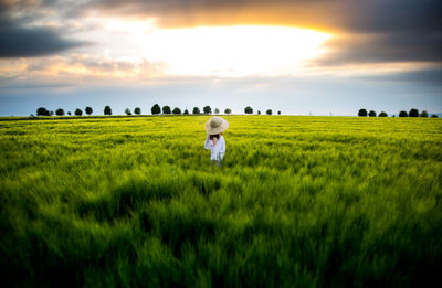 Side view of woman standing amidst plants against sky during sunset