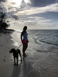 Full length of woman standing with dog on shore against sky at beach