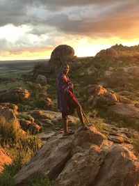 Portrait of man standing on rock against sky during sunset