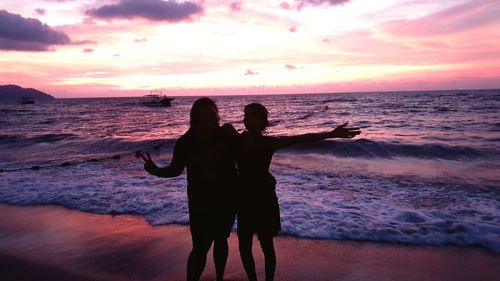 Silhouette female friends standing at beach during sunset