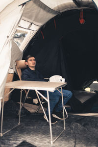 A young man is sitting at a table in a tent in a store.