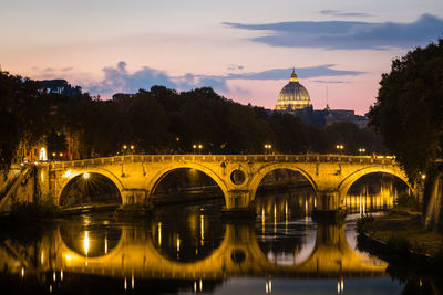 Arch bridge over river against sky at dusk