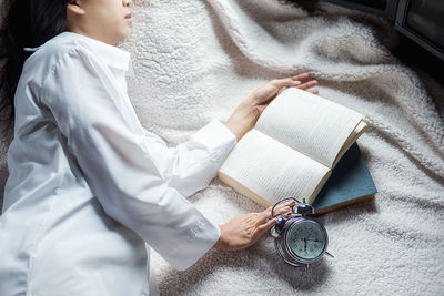 Woman with alarm clock and books sleeping on bed at home