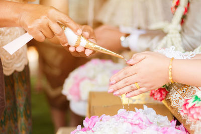 Cropped image of woman pouring water on bride clasped hands