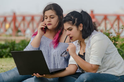 Young woman using mobile phone while sitting on laptop