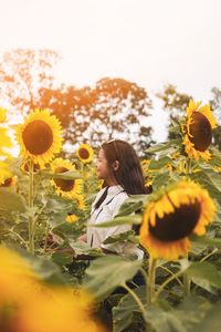 Side view of smiling woman standing amidst sunflowers on farm 