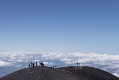 People standing on mountain against cloudy sky