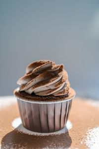 Cupcake on a dark background, that has just been sprinkled with cocoa on top.