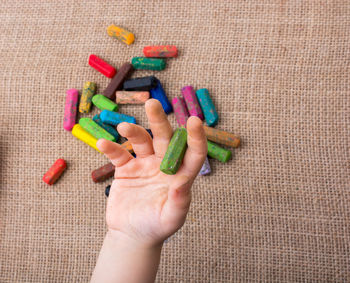 Cropped hand of child holding messy crayon on burlap