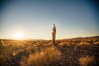 Woman standing on field against sky at sunset