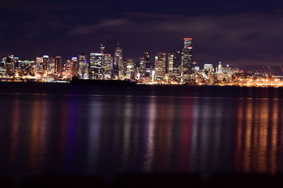 Illuminated city by sea against sky at night