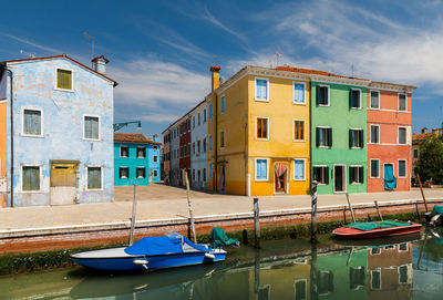 Boats moored on canal by buildings against sky