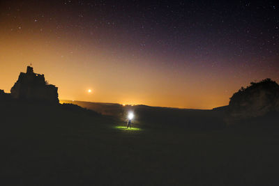 Man holding flashlight while standing on grass against sky at night