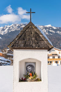 The mountain chapel with cross covered with wooden shingle. snow-capped mountains, blue sky
