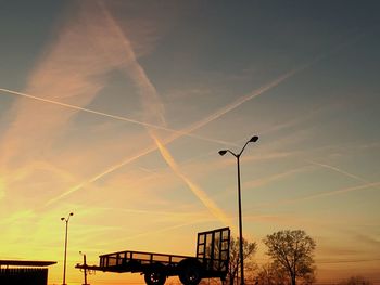 Silhouette pushcart by street lights against orange sky