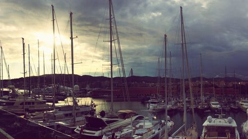 Boats moored at harbor against cloudy sky