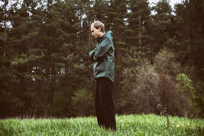 Side view of man standing on grassy field in forest