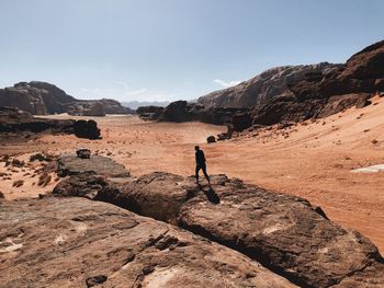 Man walking on rocks by mountains against sky