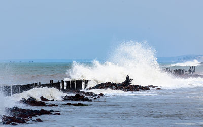 Waves splashing on shore against clear sky