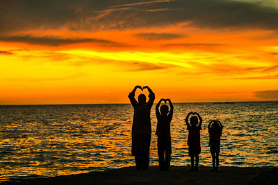 Silhouette people standing by sea against sky during sunset