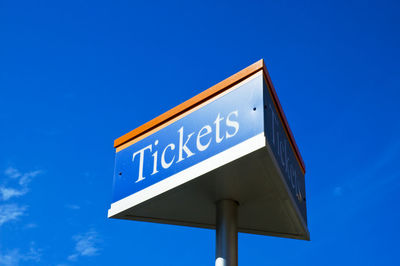 Low angle view of tickets text on metallic pole against blue sky