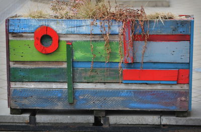 Multi colored wooden box, flower pot, similar to a  boat with red window 