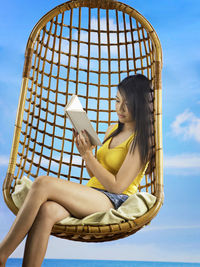Young woman reading book on wicker seat