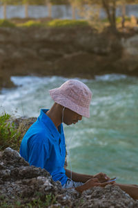 Side view of young man standing by ocean using a mobile phone