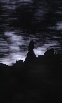 Silhouette rocks on shore against sky at dusk