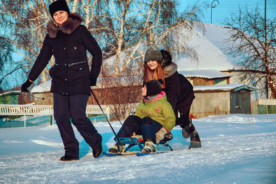 Mother and daughter sledding girl on snow covered land