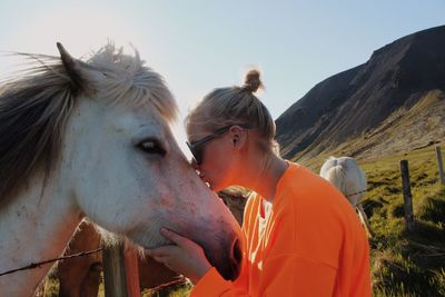 Side view of woman kissing horse against sky
