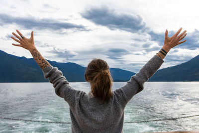 Rear view of woman with arms raised against sky