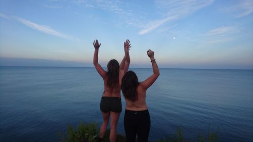 Rear view of topless female friends standing against sea