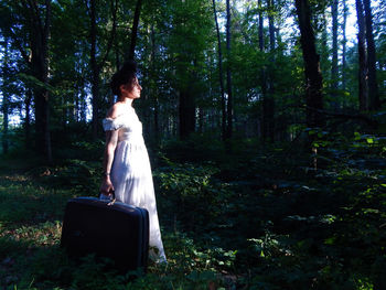 Side view of woman standing by trees in forest