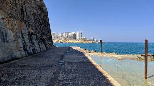 Footpath by sea against clear sky