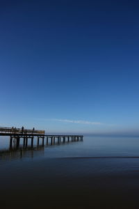 Pier over sea against clear blue sky