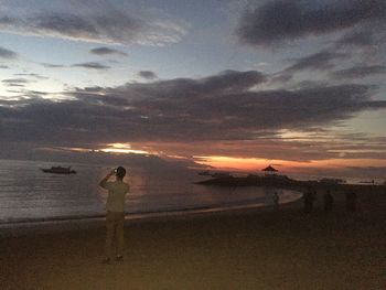 Silhouette woman standing on beach against sky during sunset