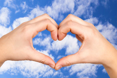 Cropped hands of woman making heart shape against blue sky