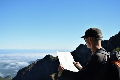 Man holding map on mountain against blue sky