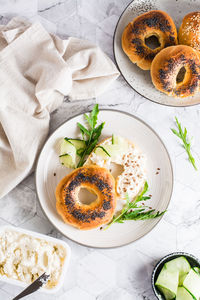 Bagel sandwich with poppy seeds with ricotta, cucumber and arugula on a plate on the table. 