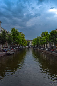 Canal amidst trees against sky in city